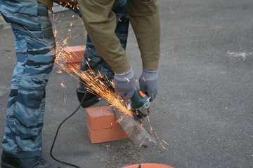 man in ordinary clothes and protective glasses with angle grinders while working in the workshop cutting metal