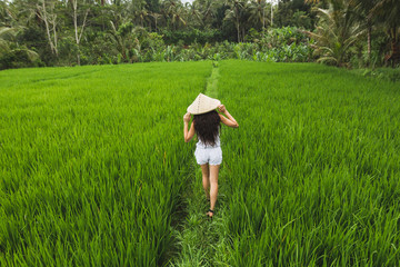 Brunette european woman walking in rice fields with traditional balinese straw hat in Ubud