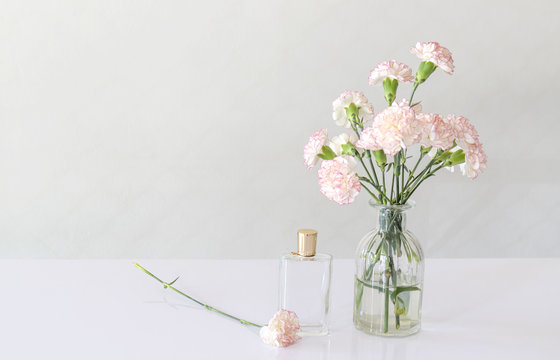 perfume bottle with carnation flowers vase on white table.