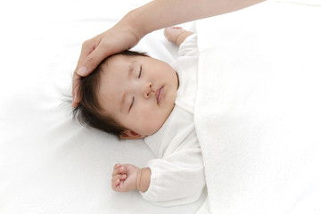 寝ている新生児に手を添え撫でる母の手