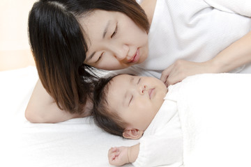新生児と添い寝しながら赤ちゃんを見つめる母