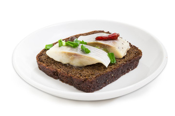 Open sandwich with pickled herring slices on brown bread closeup