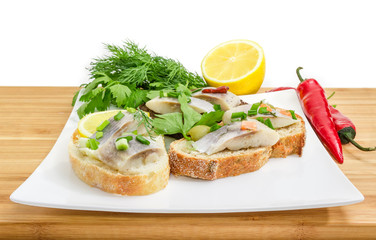 Various open sandwiches with pickled herring fillet on dish closeup