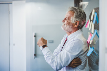 Old senior business man happy working in office, reading sticky note post it in room