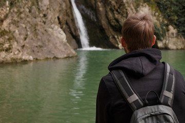 Hiker hiking with backpack looking at waterfall in sochi. Portrait of male adult back sitting outdoor.