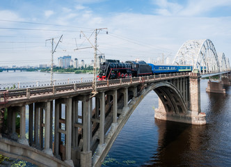 Steam locomotive with passenger train in motion on bridge