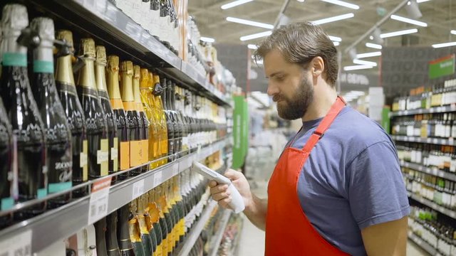 supermarket employee in red aport scanning barcode at wine section in supermarket