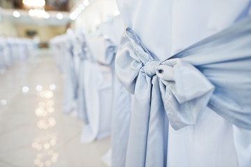 Close-up photo of big blue bows tied on white wedding chairs.