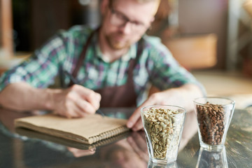 Two glasses of coffee beans, raw and roasted on table in modern roastery with blurred form of barista taking notes in background, copy space