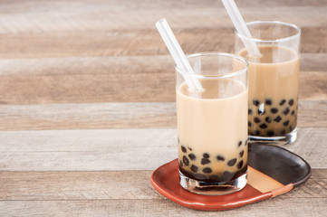 A glass of sweet milk bubble tea with tapioca pearls, and straw on wooden background. Copy space