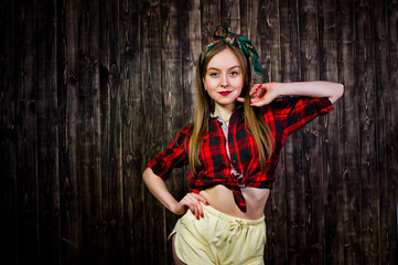 Obraz premium Young funny housewife in checkered shirt and yellow shorts pin up style on wooden background.