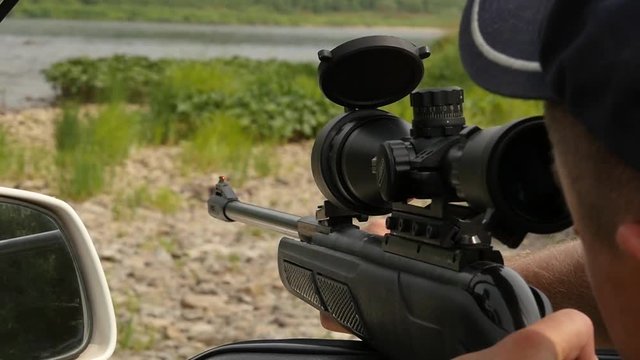 Man shooting an air rifle gun with optical sight during a vacation on a wild nature. slow motion
