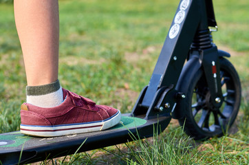 Naklejka premium Kid in casual wear on kick scooter in park