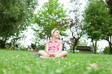 Naklejka na ściany i meble Happy teenager girl sitting on the grass in the park next to her bicycle