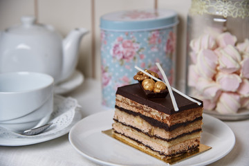 The cake with nuts is near the kettle, cup and jar with marshmallows.