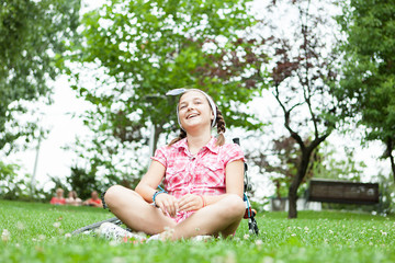 Naklejka na ściany i meble Happy teenager girl sitting on the grass in the park next to her bicycle