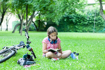 Girl reading a good book in the park next to her bicycle 