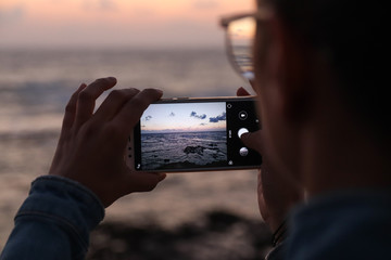 A young woman photographs with her smart phone a sunset at sea  