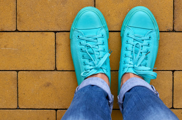 Close up photo of a girl's leg in blue sneakers on the paving background.