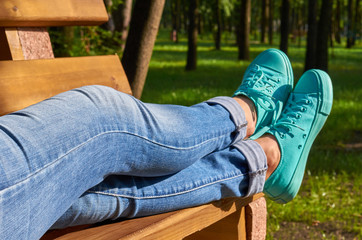 Close up photo of a girl's leg in blue sneakers on the bench background.