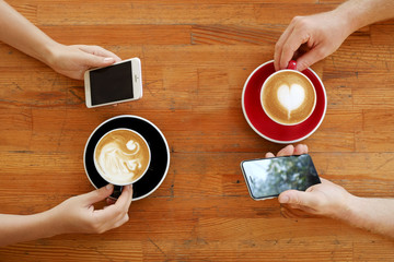 Young couple on boring date at coffee shop constantly checking phone. Man & woman drinking...