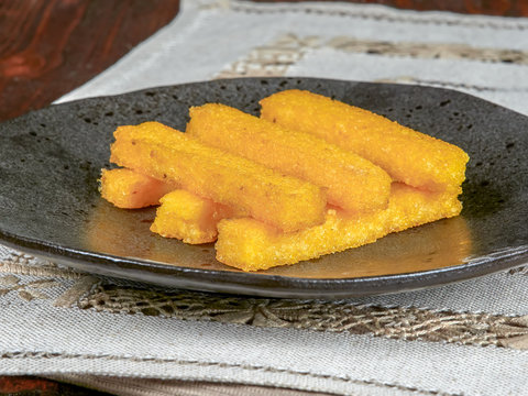 Fried polenta fingers set on a dark brown plate. A Romanian speciality.