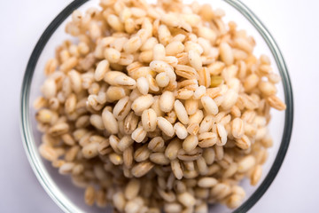 Raw and cooked Barley pearl seeds in a bowl or over white plate. selective focus