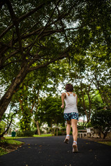 Asian woman jogging in the park, shooting from behind with big trees background