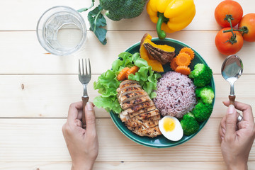 Top view woman hands eating healthy meal, Steam rice berry with grilled chicken breast, egg and vegetables.