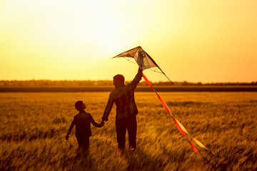 Happy father and son flying kite in the field at sunset