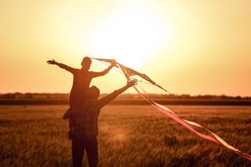 Happy father and son flying kite in the field at sunset
