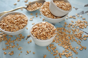 Bowls with raw oatmeal on color background
