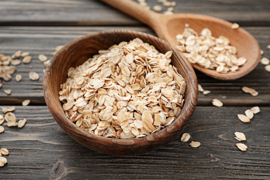 Bowl and spoon with raw oatmeal on wooden background
