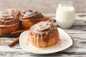 Plate with tasty cinnamon bun on wooden table
