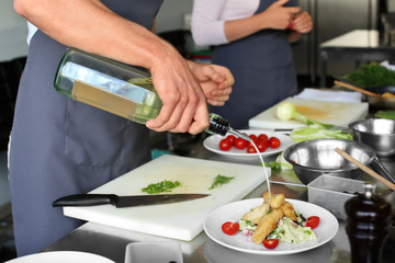 Chef preparing fried meat with salad for serving in restaurant kitchen