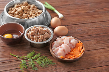Bowls with pet food and natural products on wooden background