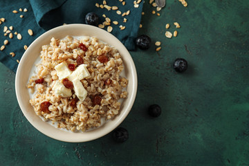 Bowl with tasty oatmeal and raisins on green table