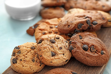 Wooden board with delicious chocolate chip cookies on table