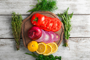 Board with different fresh herbs, lemon and vegetables on wooden background