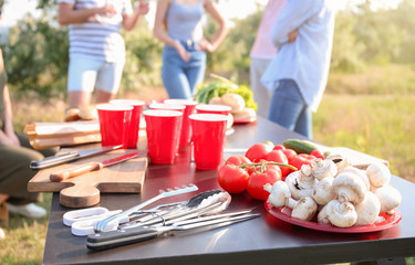 Table with products for barbecue and company of friends outdoors