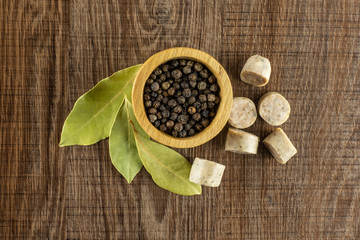 Lot of slices of bavarian white sausage with black pepper in a wooden bowl and three bay laurel leaves flatlay on brown wood