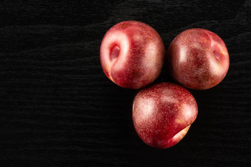 Fototapeta na wymiar Group of three whole fresh pluot interspecific plums variety flatlay on black wood
