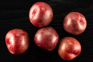 Fototapeta na wymiar Group of five whole fresh pluot interspecific plums variety flatlay on black wood