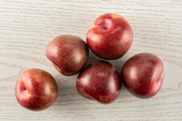 Group of five whole fresh pluot interspecific plums variety flatlay on grey wood