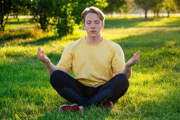 handsome young man in a yellow t-shirt is engaged in yoga in the park on a sunny day