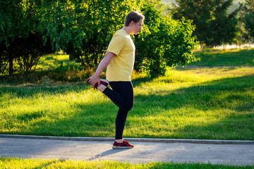 handsome young man in a yellow t-shirt doing stretching in the park on a sunny day