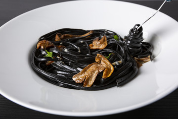 Pasta with wheat germ and black squid ink. Mushroom sauce. Olive oil and spices. Action in the frame. Spaghetti is wrapped around a fork.
