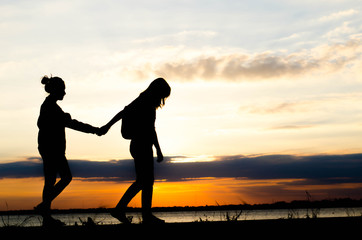 Silhouette of woman walking holding hand during a beautiful sunset.