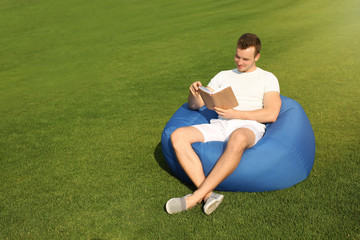 Young man reading book while sitting on bean bag chair outdoors