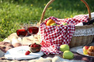 Basket with food and glasses of wine on plaid prepared for romantic picnic in park